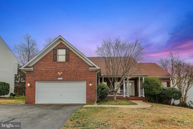 traditional-style home with an attached garage, brick siding, aphalt driveway, a front yard, and covered porch