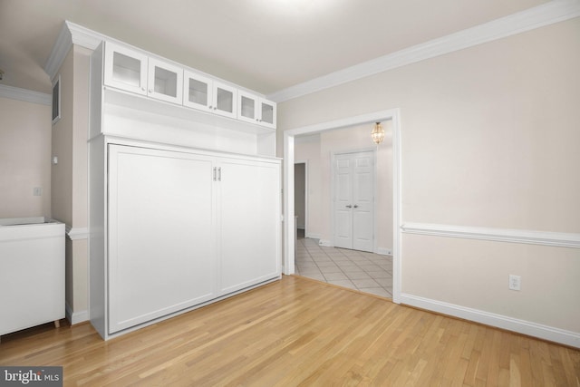 interior space with light wood-type flooring, ornamental molding, baseboards, and a closet