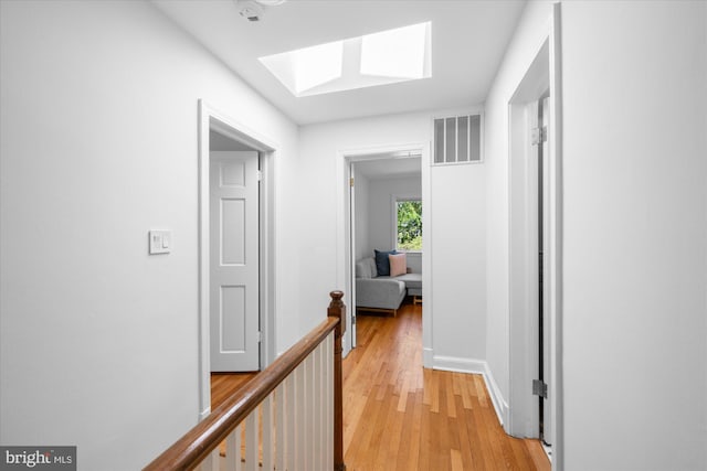 hallway featuring visible vents, a skylight, baseboards, an upstairs landing, and light wood-style floors
