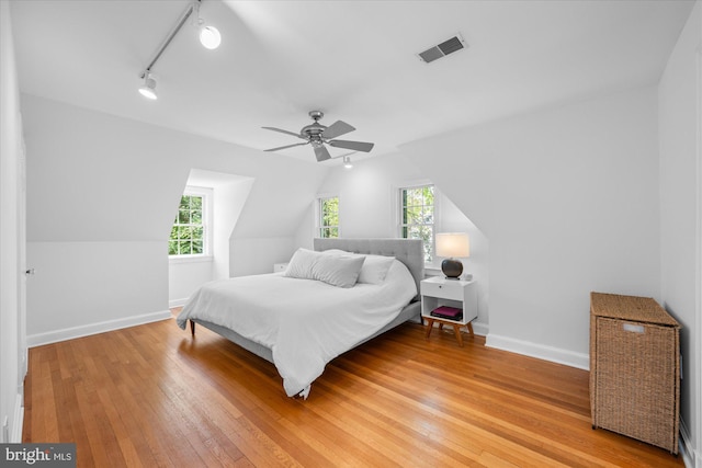 bedroom with track lighting, light wood finished floors, baseboards, lofted ceiling, and visible vents