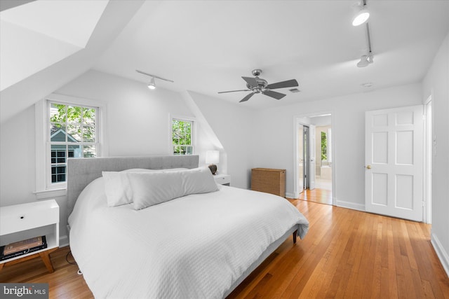 bedroom with ceiling fan, track lighting, light wood-style floors, baseboards, and ensuite bathroom