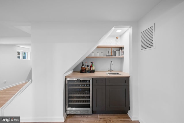 bar with a sink, beverage cooler, light wood-style flooring, baseboards, and wet bar