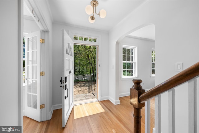 entryway with ornamental molding, baseboards, arched walkways, light wood-style flooring, and a notable chandelier