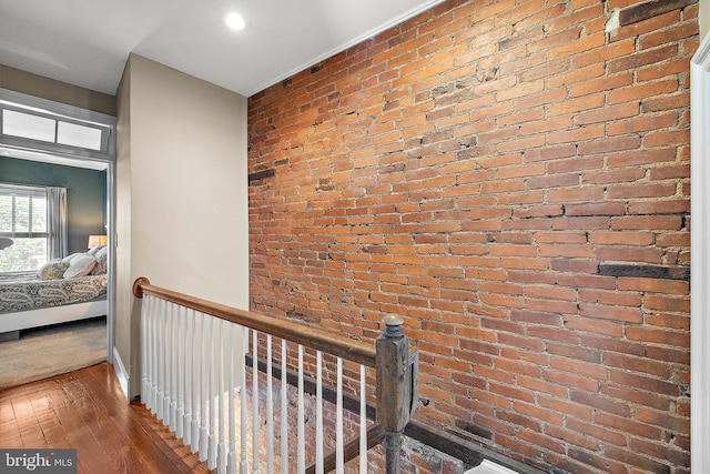 hall featuring brick wall, an upstairs landing, and hardwood / wood-style flooring