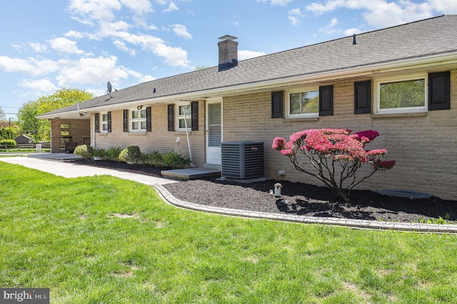 exterior space featuring a chimney, central AC unit, brick siding, and a front yard