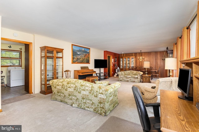 carpeted living area featuring washer / dryer, a notable chandelier, and wooden walls