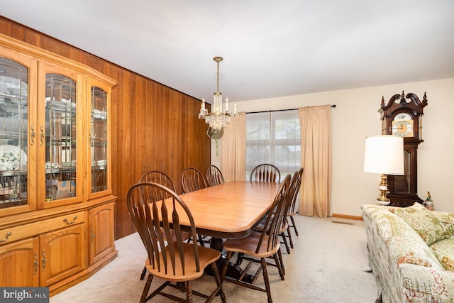 dining room with an inviting chandelier, light carpet, and wood walls