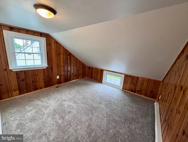 additional living space with healthy amount of natural light, wood walls, vaulted ceiling, and carpet flooring