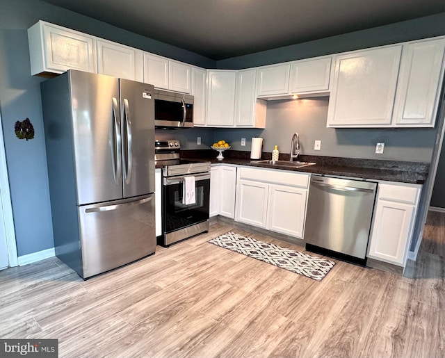 kitchen with stainless steel appliances, a sink, light wood finished floors, and white cabinets