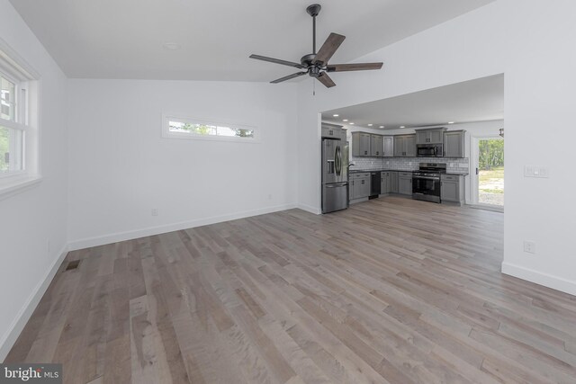 unfurnished living room with ceiling fan, visible vents, vaulted ceiling, baseboards, and light wood-style flooring