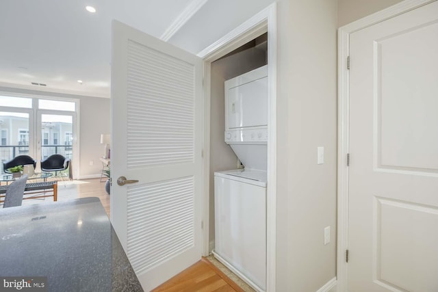 laundry area featuring laundry area, light wood-style floors, recessed lighting, baseboards, and stacked washer / dryer