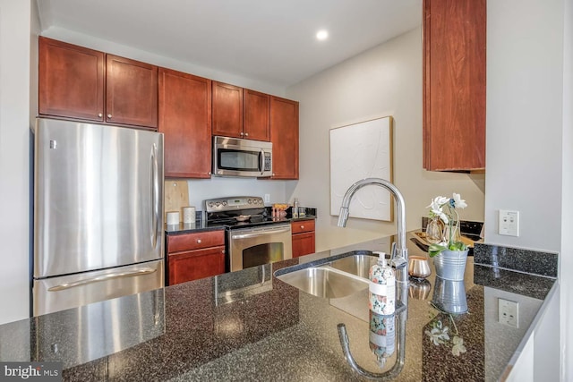 kitchen featuring reddish brown cabinets, a sink, dark stone counters, and appliances with stainless steel finishes