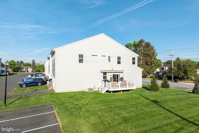rear view of house with a yard, a wooden deck, and uncovered parking
