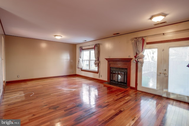 unfurnished living room featuring baseboards, a glass covered fireplace, visible vents, and light wood-type flooring
