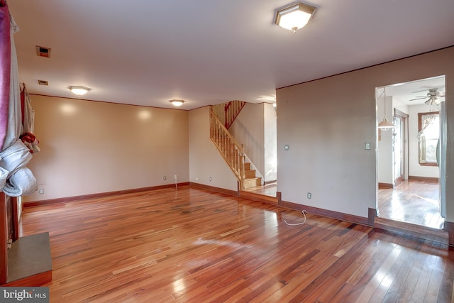 unfurnished living room featuring baseboards, a ceiling fan, stairs, and light wood-style flooring