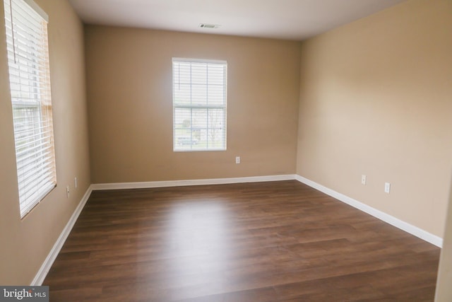 unfurnished room featuring baseboards, a wealth of natural light, dark wood finished floors, and visible vents