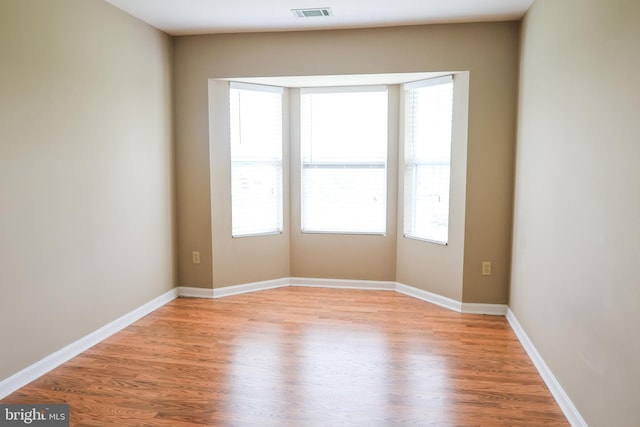 empty room with baseboards, visible vents, plenty of natural light, and light wood-style floors