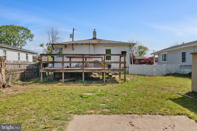 back of house with a lawn, a wooden deck, a fenced backyard, and a chimney