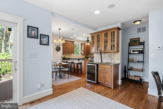 kitchen featuring a sink, brown cabinetry, wine cooler, backsplash, and visible vents