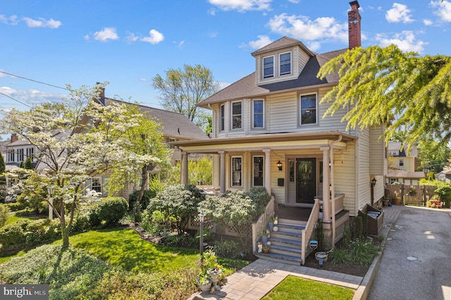 traditional style home with a porch, a shingled roof, fence, and a chimney