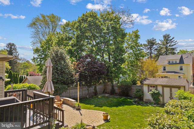 view of yard with a storage shed, a wooden deck, an outdoor structure, a fenced backyard, and a patio