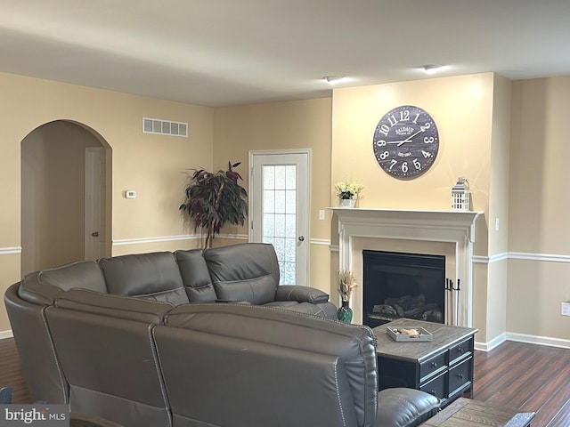 living room with visible vents, dark wood-style flooring, a glass covered fireplace, baseboards, and arched walkways