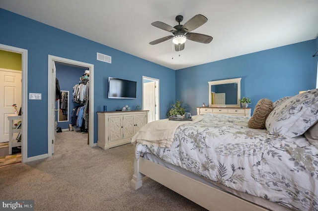 carpeted bedroom featuring visible vents, a closet, baseboards, a walk in closet, and a ceiling fan