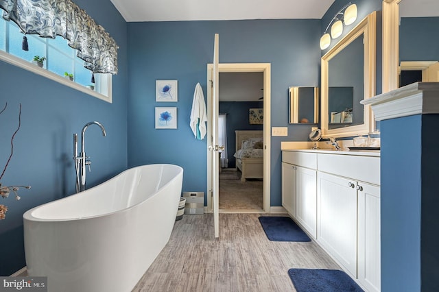 full bath with connected bathroom, vanity, a freestanding tub, baseboards, and wood finished floors