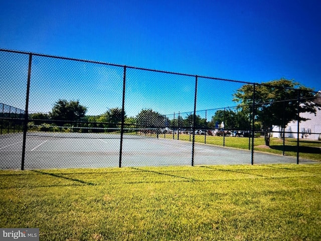 view of tennis court featuring a lawn and fence