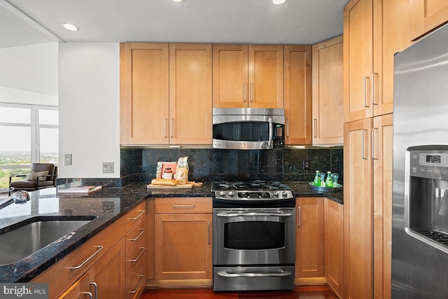 kitchen with appliances with stainless steel finishes, tasteful backsplash, a sink, and dark stone countertops