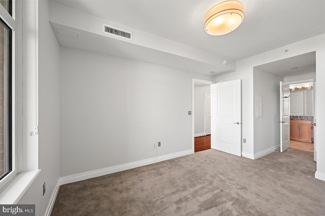 unfurnished bedroom with visible vents, baseboards, carpet floors, and ensuite bathroom