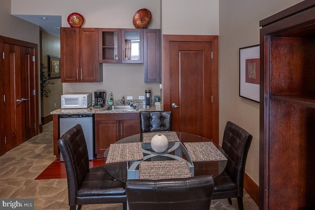 kitchen featuring dishwasher, a sink, white microwave, glass insert cabinets, and carpet flooring