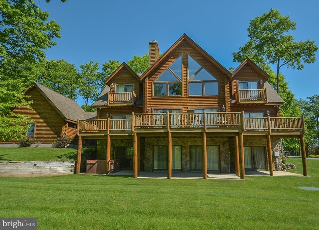 rear view of house featuring a yard, a chimney, stone siding, and a wooden deck
