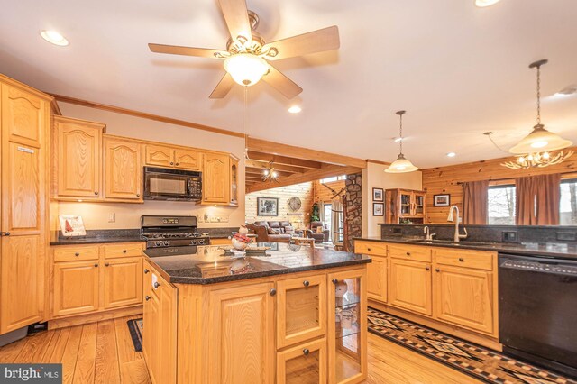 kitchen featuring dark stone countertops, a sink, light wood finished floors, black appliances, and hanging light fixtures