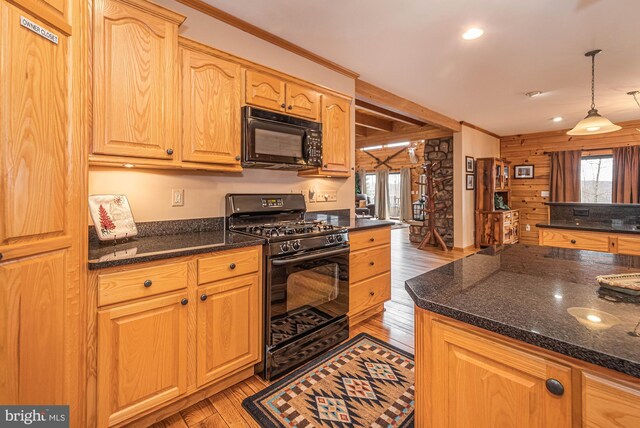 kitchen with dark stone countertops, hanging light fixtures, black appliances, and light wood-style floors