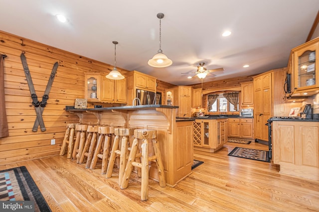 kitchen with dark countertops, ceiling fan, stainless steel refrigerator, a peninsula, and a kitchen bar