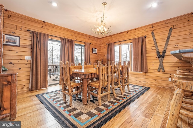 dining space featuring light wood-type flooring, a notable chandelier, and wooden walls