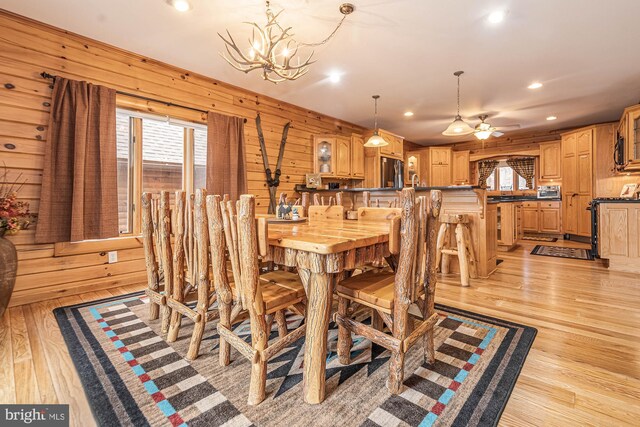 dining space with recessed lighting, wood walls, light wood finished floors, and ceiling fan with notable chandelier