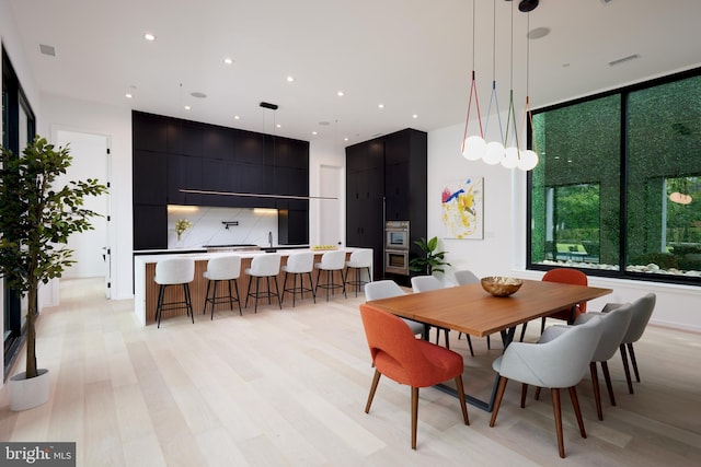 dining room featuring light wood-style floors, visible vents, and a towering ceiling