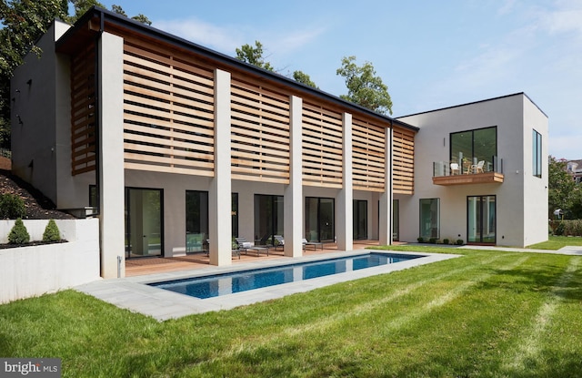 back of property featuring a yard, an outdoor pool, stucco siding, and a balcony