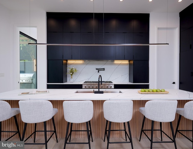 kitchen featuring light stone countertops, modern cabinets, tasteful backsplash, dark cabinets, and a sink