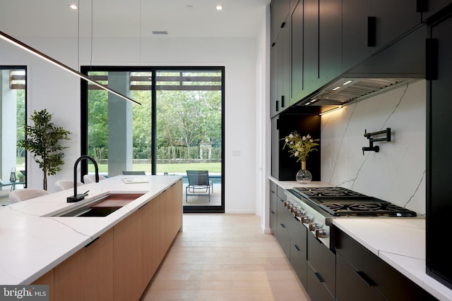 kitchen featuring light stone counters, a sink, light wood finished floors, stainless steel gas stovetop, and modern cabinets
