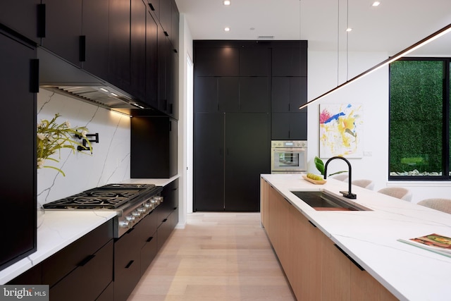 kitchen featuring dark cabinetry, stainless steel appliances, a sink, and light wood-type flooring