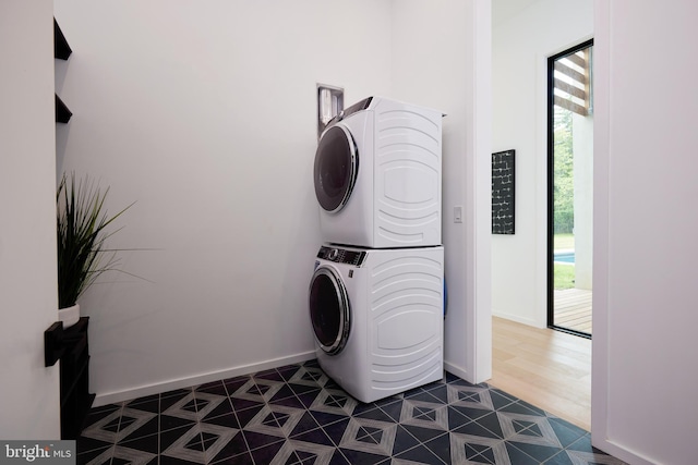 laundry area featuring stacked washing maching and dryer, baseboards, laundry area, and a healthy amount of sunlight