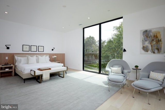 bedroom with light wood-style floors, access to exterior, and a wall of windows