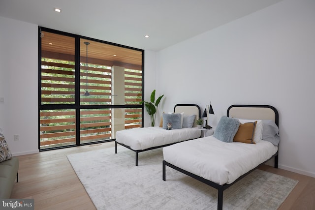 bedroom with baseboards, floor to ceiling windows, recessed lighting, and wood finished floors