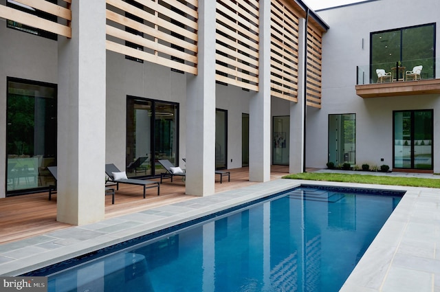 exterior space featuring a balcony, a patio, stucco siding, and an outdoor pool