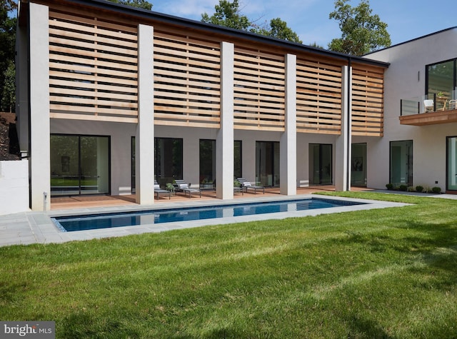 back of house with an outdoor pool, a balcony, a yard, a patio, and stucco siding