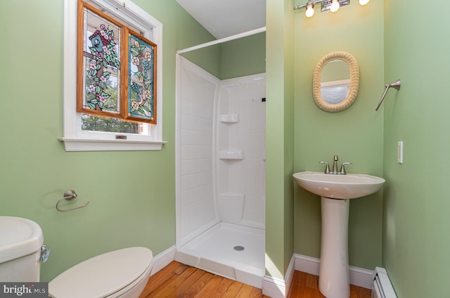 bathroom with toilet, wood finished floors, a stall shower, baseboard heating, and baseboards