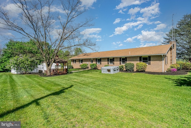 rear view of property with a yard, a gazebo, a chimney, and brick siding